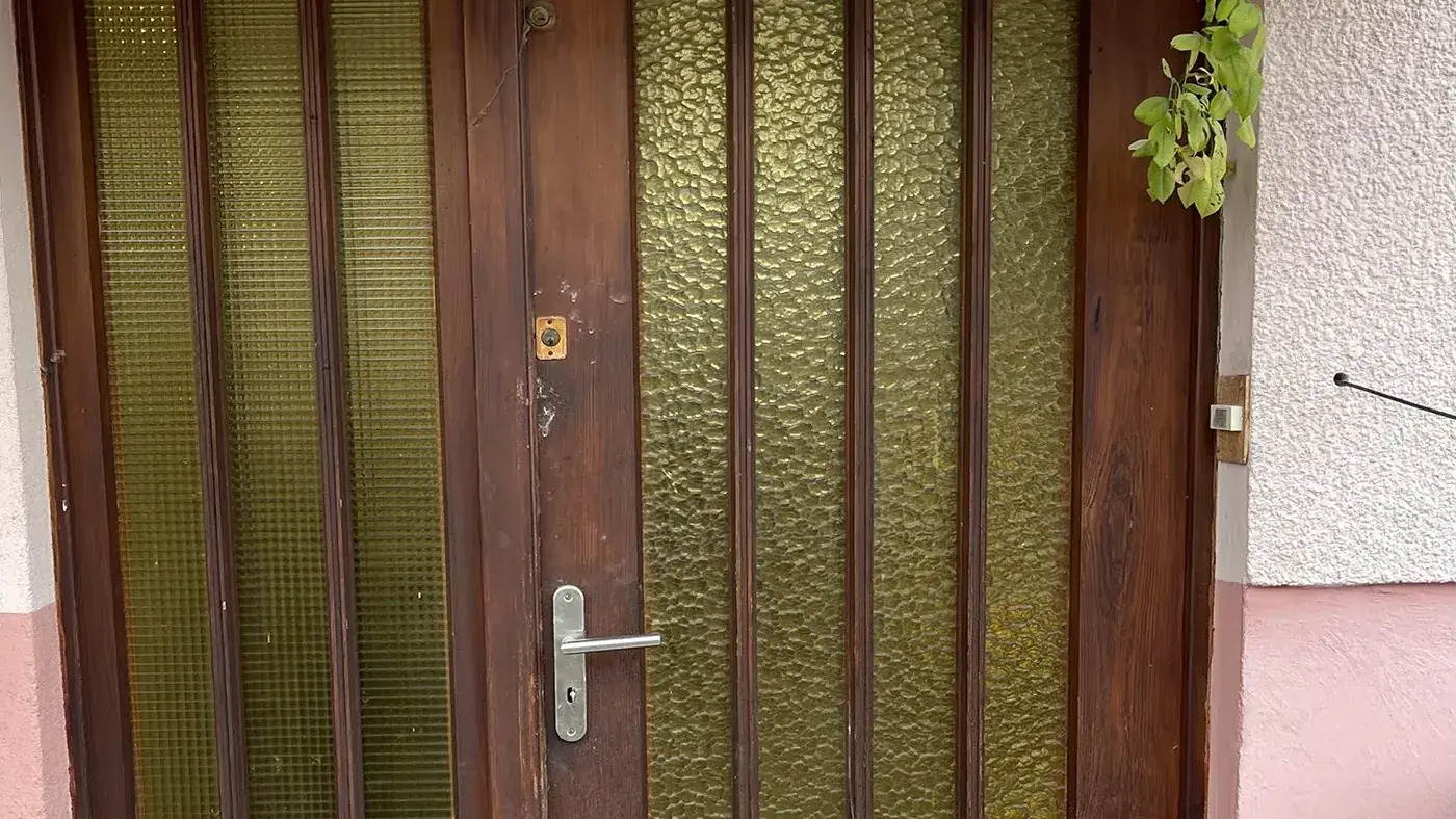 Porte d'entrée en bois foncé d'origine, vitrages cannelés et quincaillerie vieillissante