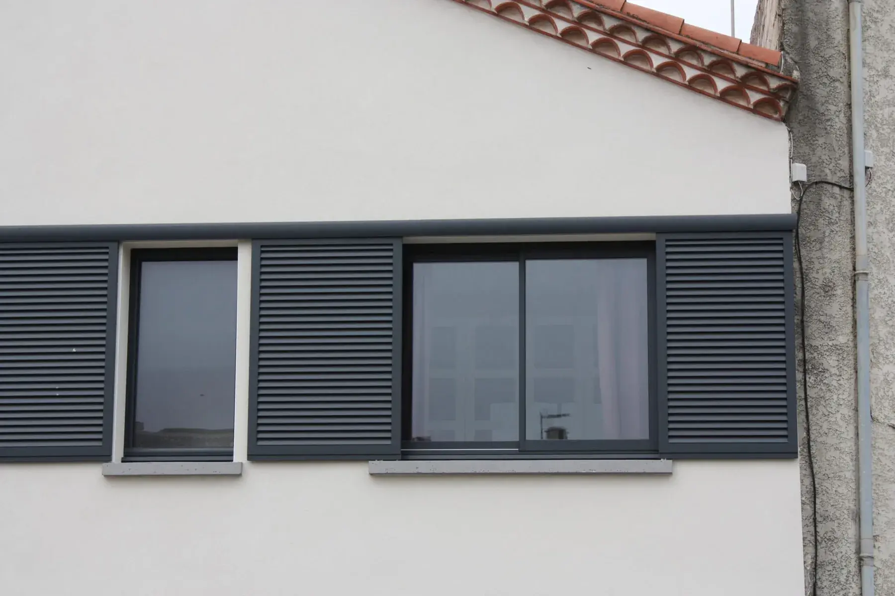 Bandeau de fenêtres anthracite avec volets roulants sur une façade beige