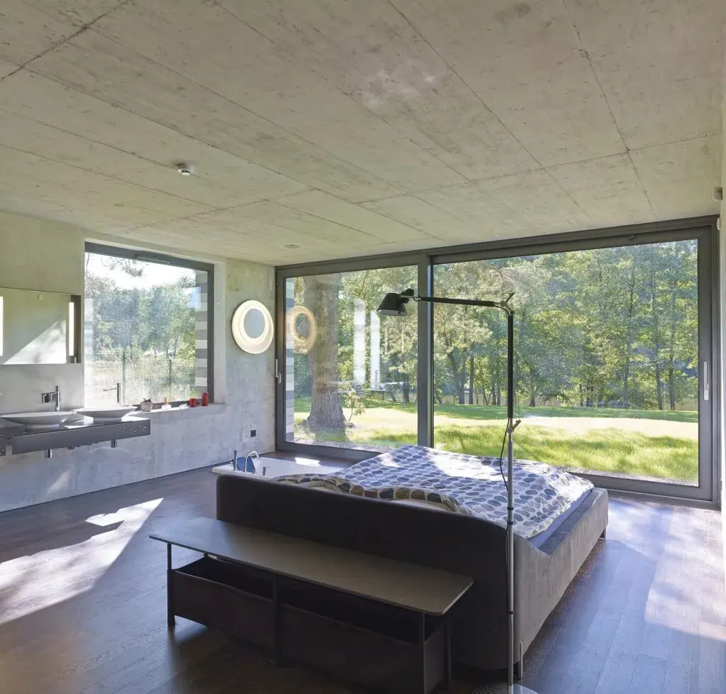 Chambre contemporaine à plafond de béton brut, avec baie vitrée d'angle et hublots ronds