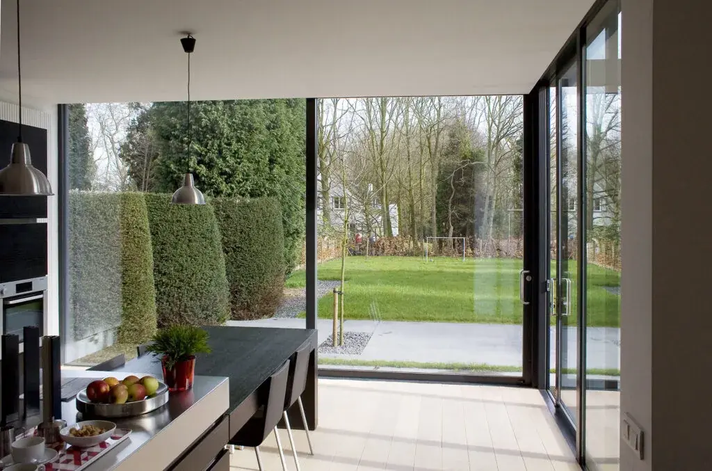 Cuisine ouverte sur un jardin clos de haies par une baie coulissante aluminium