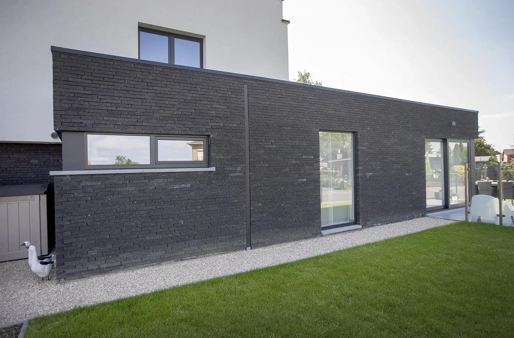 Extension contemporaine à bardage noir avec bandeau vitré filant donnant sur une pelouse