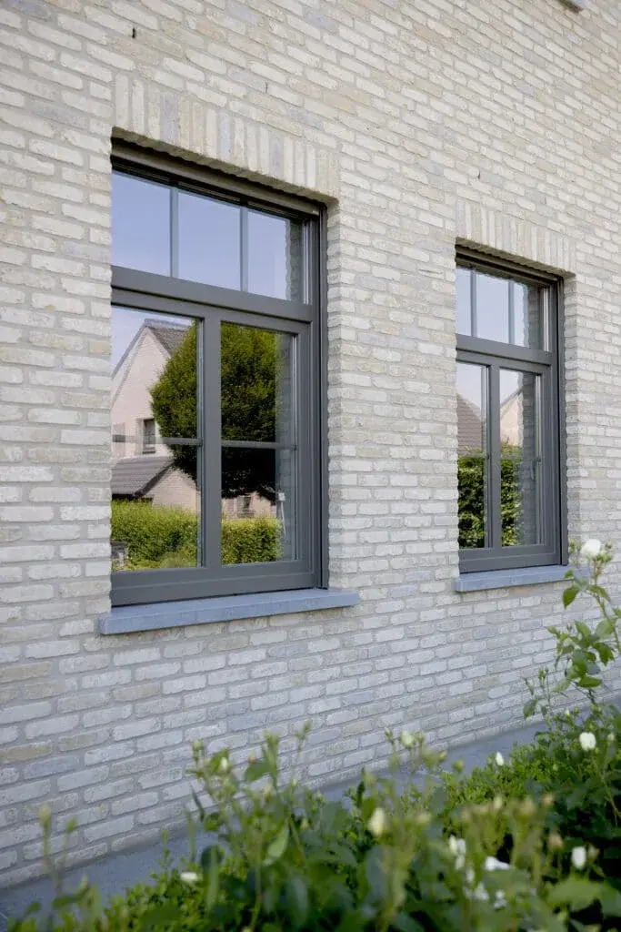 Deux fenêtres anthracite posées dans une façade de brique claire