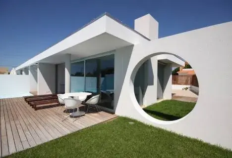 Maison contemporaine blanche percée d'une grande ouverture circulaire sur une terrasse en bois