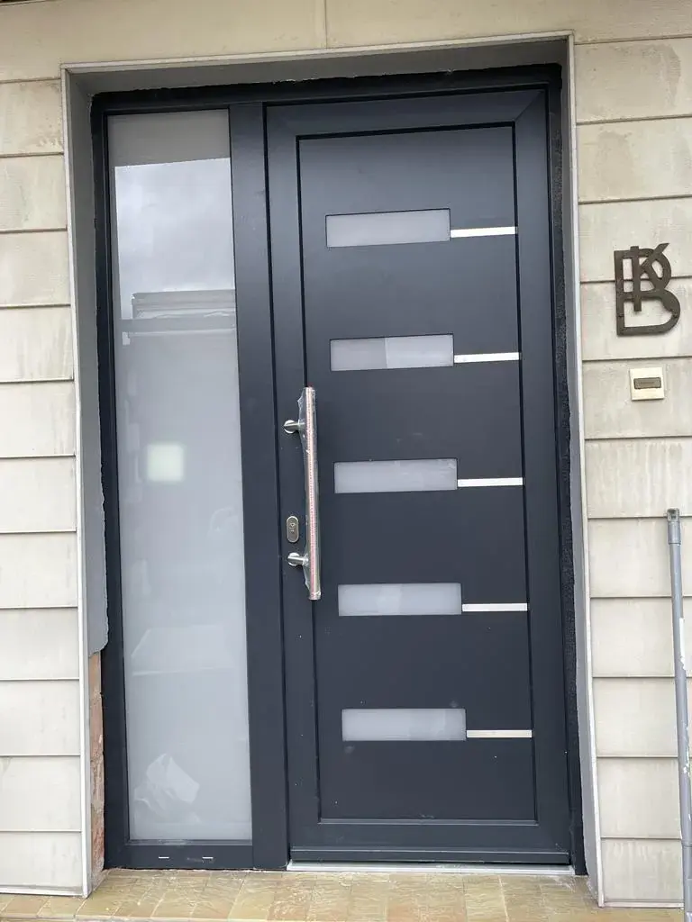 Porte d'entrée aluminium anthracite à inserts inox et poignée barre, façade en pierre claire