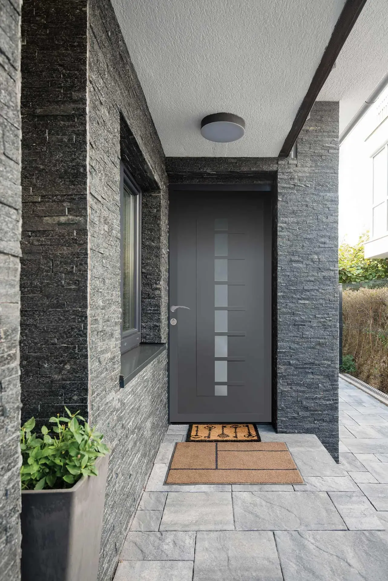Porte d'entrée anthracite abritée sous un auvent, mur en pierre naturelle