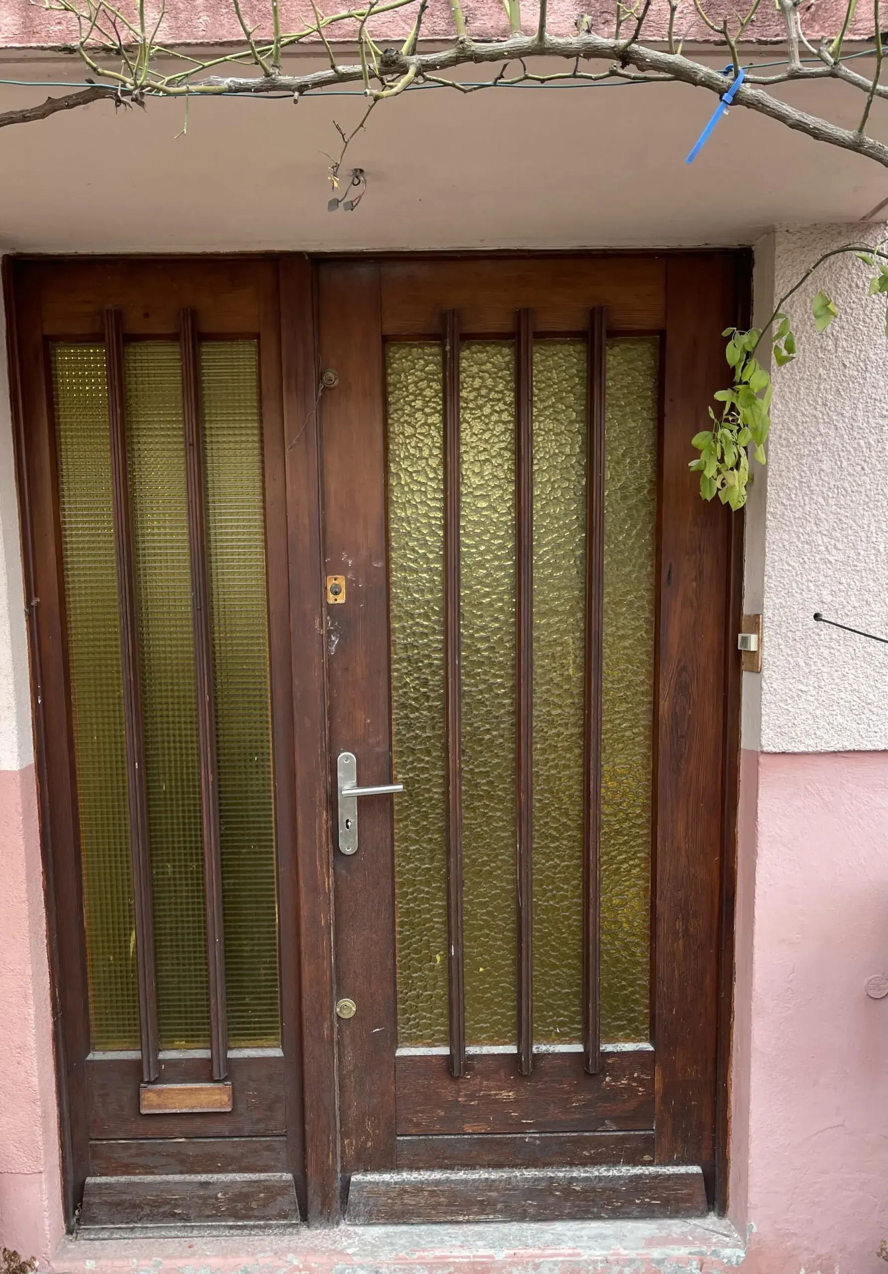 Porte d'entrée en bois foncé d'origine avec vitrages cannelés, façade rose