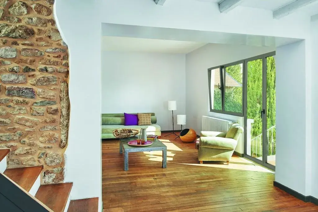 Séjour avec mur en pierre apparente, parquet et grande baie ouvrant sur un jardin